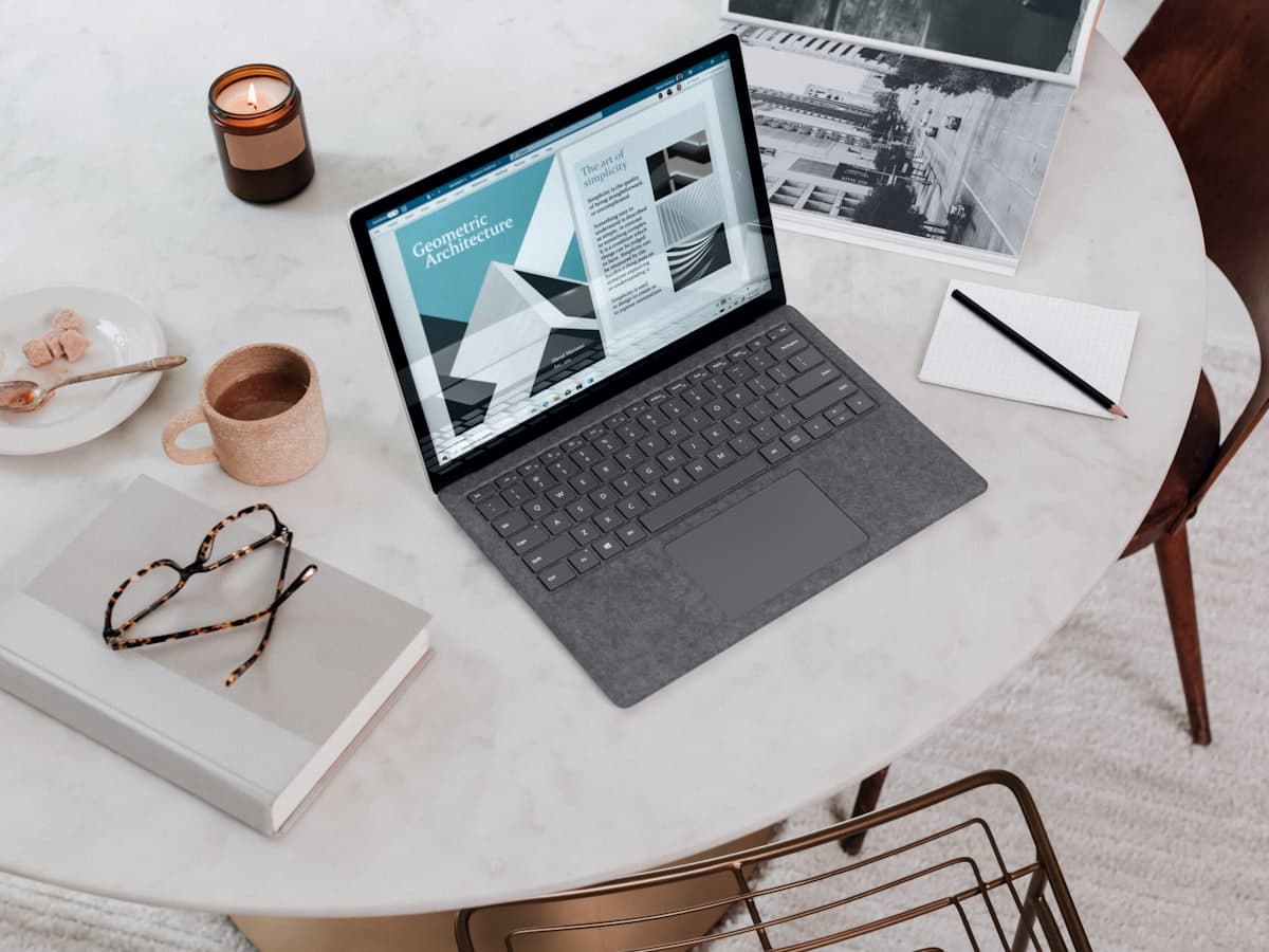 A laptop open on a pale stone table beside a notebook
